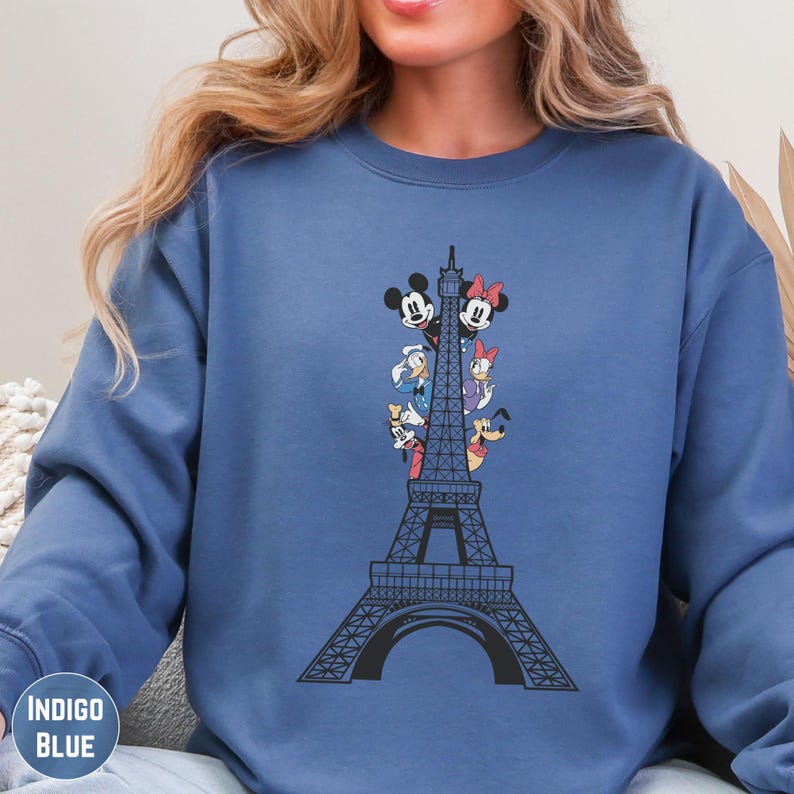 A woman wearing a blue sweatshirt with a graphic of the Eiffel Tower and Disney characters on it.