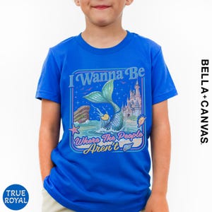 A young boy wearing a blue t-shirt with a mermaid graphic and text.
