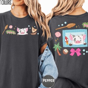 a woman wearing a black t-shirt with a colorful graphic design on the back. The design includes a pig, palm tree, starfish, and other whimsical elements.