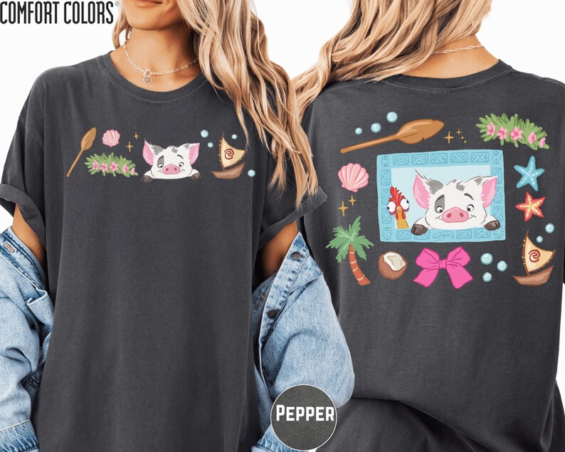 a woman wearing a black t-shirt with a colorful graphic design on the back. The design includes a pig, palm tree, starfish, and other whimsical elements.