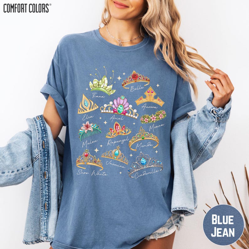 A woman wearing a blue t-shirt with a graphic design of various crowns and tiaras, along with the text "Comfort Colors" printed on it.
