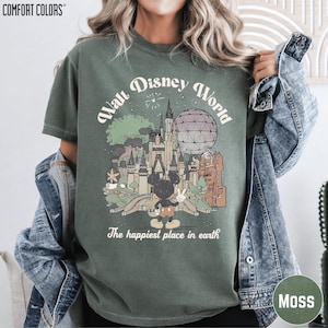 A woman wearing a green t-shirt with a graphic design of Disney World, including Mickey Mouse and various landmarks, and the text "The happiest place in earth".