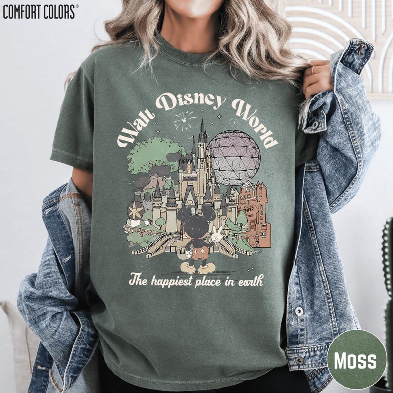 A woman wearing a green t-shirt with a graphic design of Disney World, including Mickey Mouse and various landmarks, and the text "The happiest place in earth".