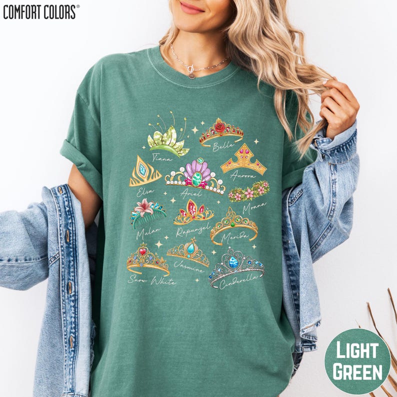 A woman wearing a green t-shirt with a design of various crowns and tiaras printed on it.