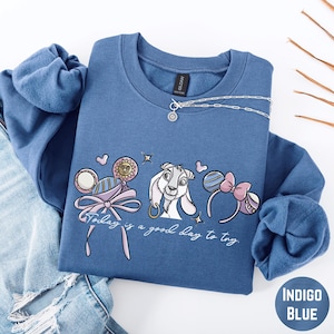 A blue sweatshirt with a cartoon character and text printed on it, along with a necklace and some accessories.