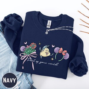 A navy blue sweatshirt with a colorful graphic design featuring a cartoon character and the text "Part of your world" printed on it.