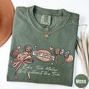 a green t-shirt with a cartoon character design, a necklace, and some decorative elements such as leaves and a hat.