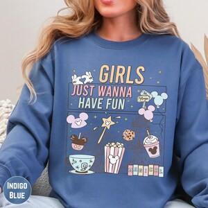 A woman wearing a blue sweatshirt with a graphic design featuring various Disney-themed items and text.