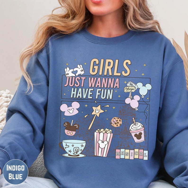 A woman wearing a blue sweatshirt with a graphic design featuring various Disney-themed items and text.