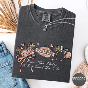 a gray t-shirt with a graphic design, a pair of jeans, and some accessories such as a necklace and a bracelet.