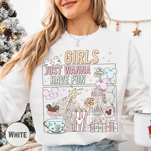 A woman wearing a white sweatshirt with a colorful graphic design featuring various Disney-themed items and text.
