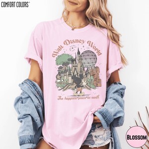 A woman wearing a pink t-shirt with a graphic of Disney World and the text "The happiest place on earth" printed on it.
