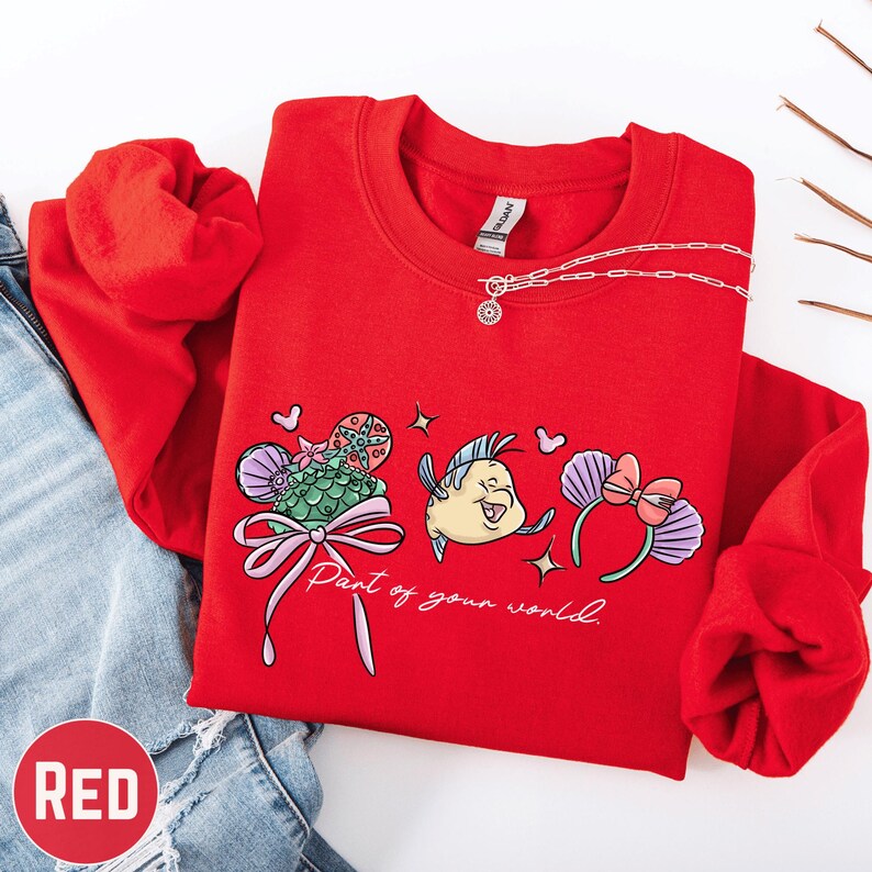 A red sweater with a cartoon character design and the text "Part of your world" printed on it, along with a necklace and a pair of jeans.