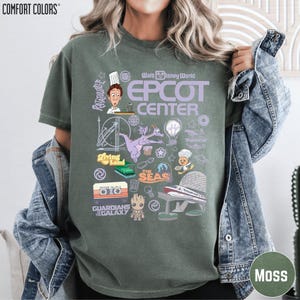 A woman wearing a green t-shirt with various Disney-themed graphics and icons, including characters, landmarks, and other iconic elements associated with the Epcot Center.