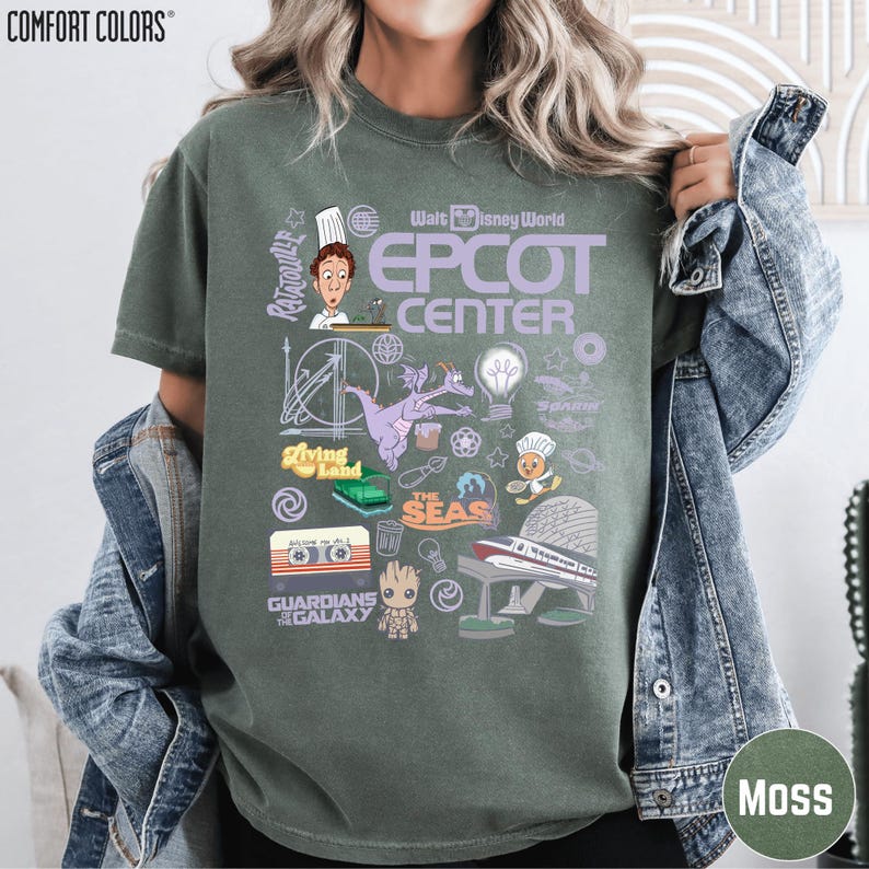 A woman wearing a green t-shirt with various Disney-themed graphics and icons, including characters, landmarks, and other iconic elements associated with the Epcot Center.