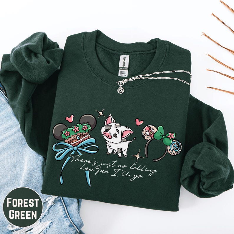 A green sweatshirt with a graphic design featuring a pig, a bow, and various Disney-themed elements, along with the text "There's just no telling how far I'll go".