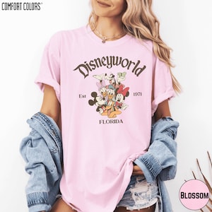 A woman wearing a pink t-shirt with a Disneyworld graphic and text, along with a denim jacket, posing against a white background.