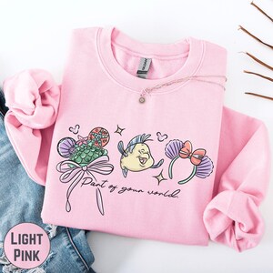 A pink sweatshirt with a cartoon character and text printed on it, along with a necklace and some other clothing items.