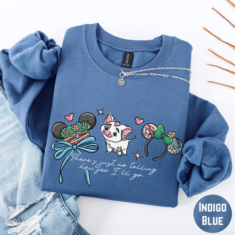 A blue sweatshirt with a cartoon pig and various Disney-themed accessories, such as Mickey Mouse ears and a bow, printed on it.