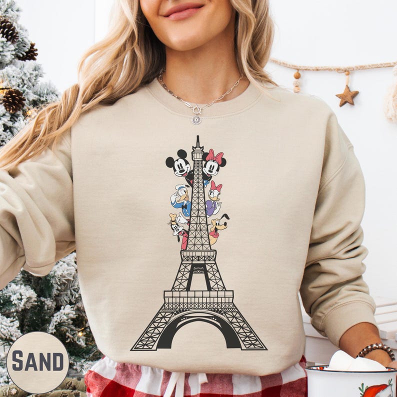 A woman wearing a beige sweater with a graphic of the Eiffel Tower and Disney characters on it.