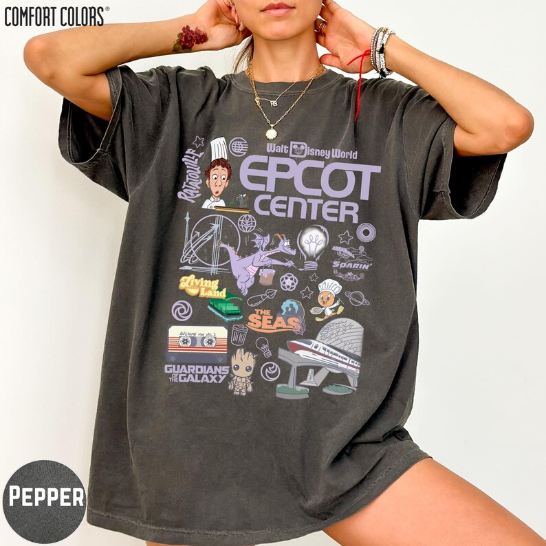 A person wearing a gray t-shirt with various Disney-themed graphics and text, including characters, landmarks, and logos associated with the Walt Disney World Epcot Center.