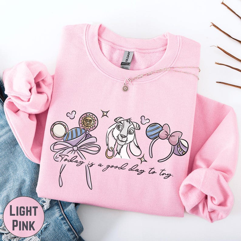 A pink sweatshirt with a cartoon character and text printed on it, along with a necklace and some other accessories.