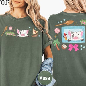 A woman wearing a green t-shirt with a cartoon pig and various other colorful elements on the front and back.