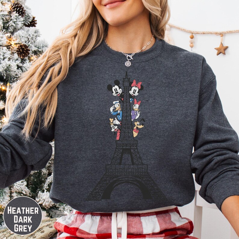 A woman wearing a gray sweatshirt with a graphic of the Eiffel Tower and Disney characters on it.