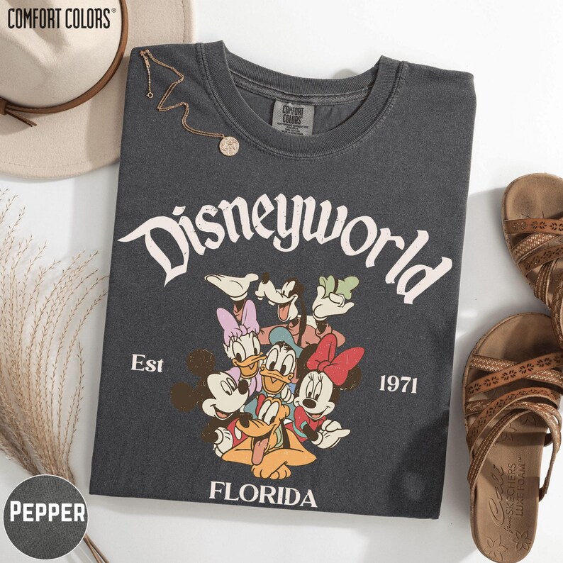 a black t-shirt with a Disneyworld graphic, a beige hat, a pair of sandals, and a necklace.