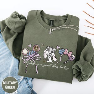 A military green sweatshirt with a graphic design featuring a cartoon character and the text "Today is a good day to try".