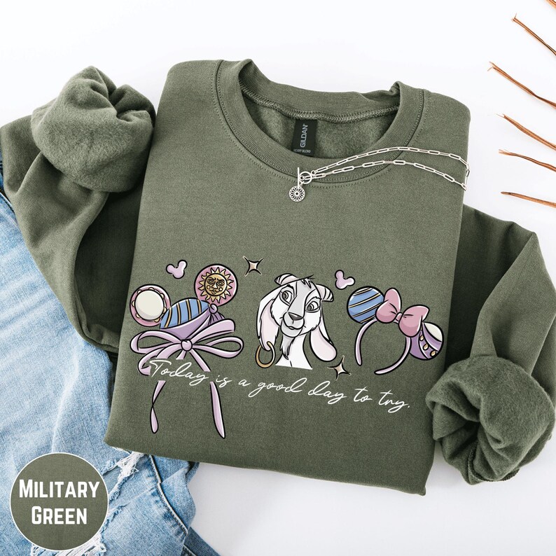 A military green sweatshirt with a graphic design featuring a cartoon character and the text "Today is a good day to try".