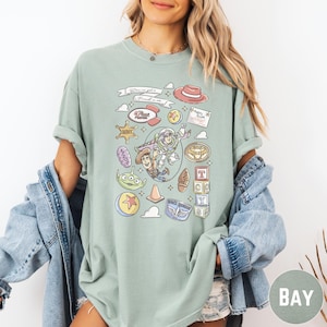 A woman wearing a green t-shirt with various cartoon characters and icons printed on it, along with a denim jacket.