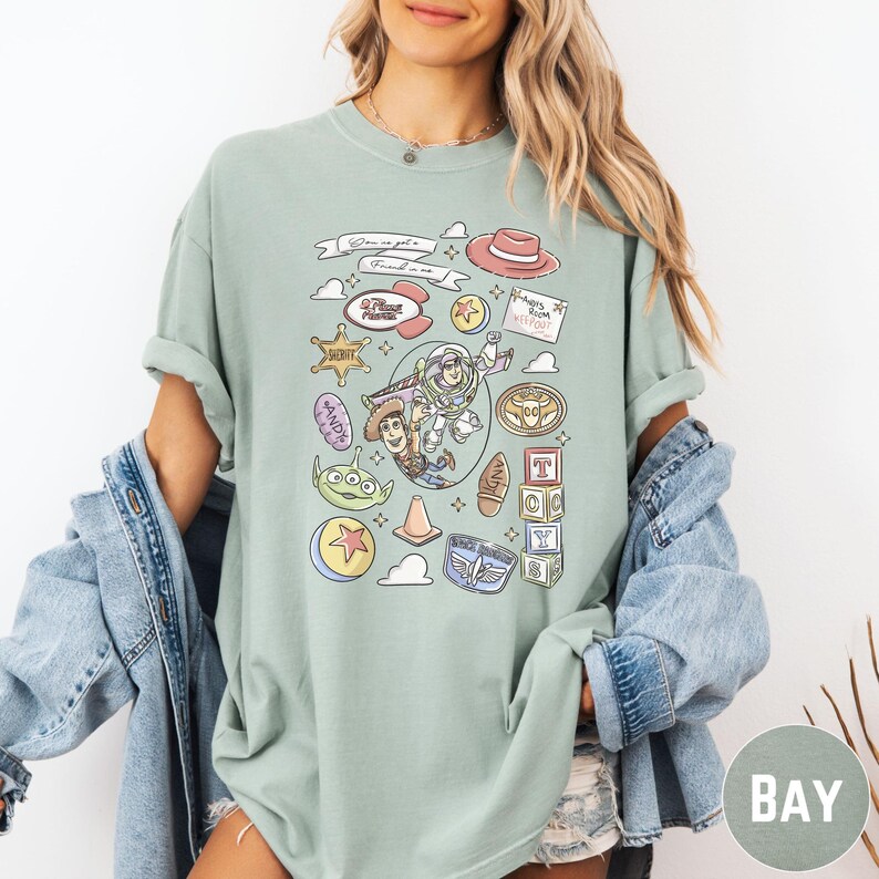 A woman wearing a green t-shirt with various cartoon characters and icons printed on it, along with a denim jacket.