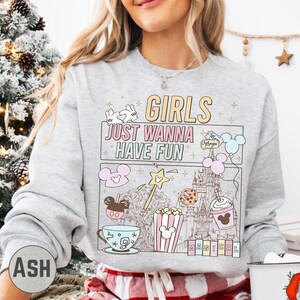 A woman wearing a gray sweatshirt with a graphic design featuring various Disney-themed items and text.