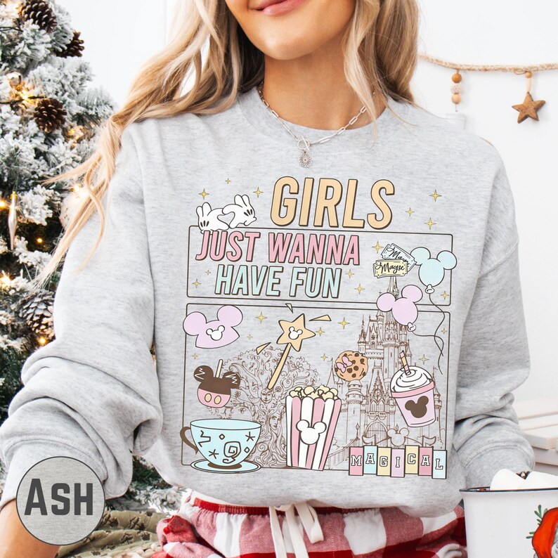 A woman wearing a gray sweatshirt with a graphic design featuring various Disney-themed items and text.