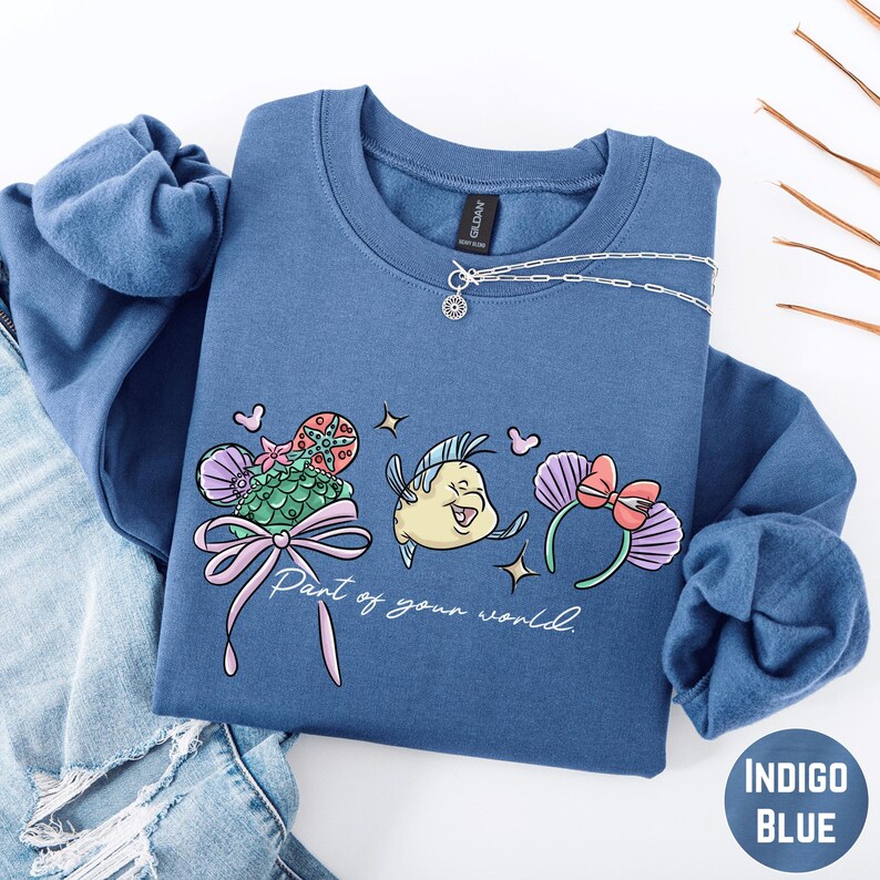 A blue sweatshirt with a cartoon fish design and the text "Part of your world" printed on it, along with a necklace and some other clothing items.