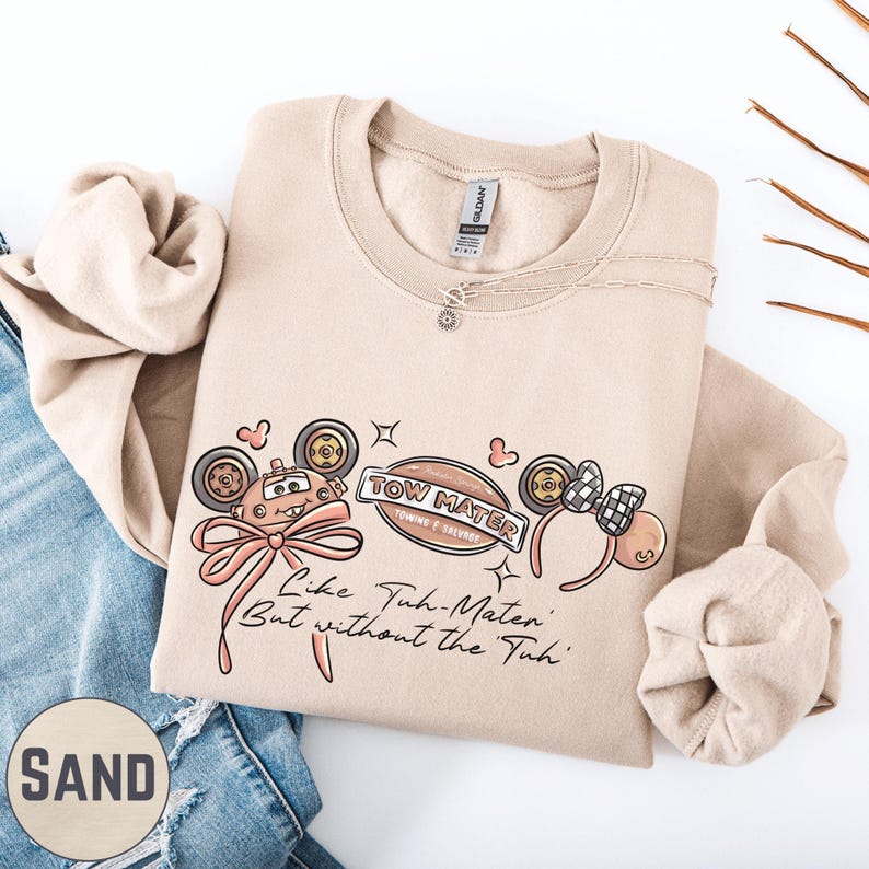 a beige sweatshirt with a graphic design, a pair of blue jeans, and some decorative elements such as a necklace and a plant.