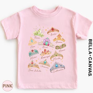 A pink t-shirt with a design of various crowns and tiaras, each with a unique color and style.