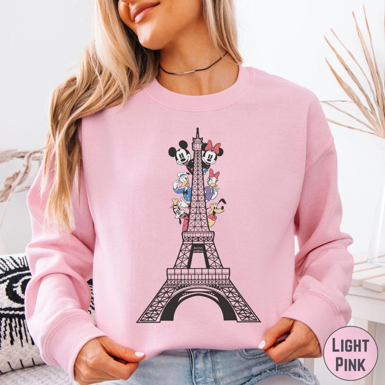 A woman wearing a pink sweatshirt with a graphic of the Eiffel Tower and Disney characters printed on it.