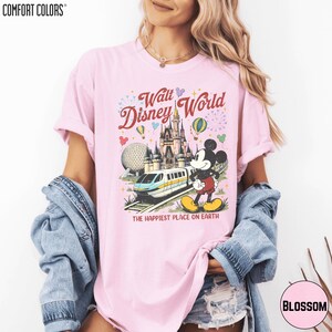 A woman wearing a pink t-shirt with a Disney World graphic and text, along with a denim jacket.