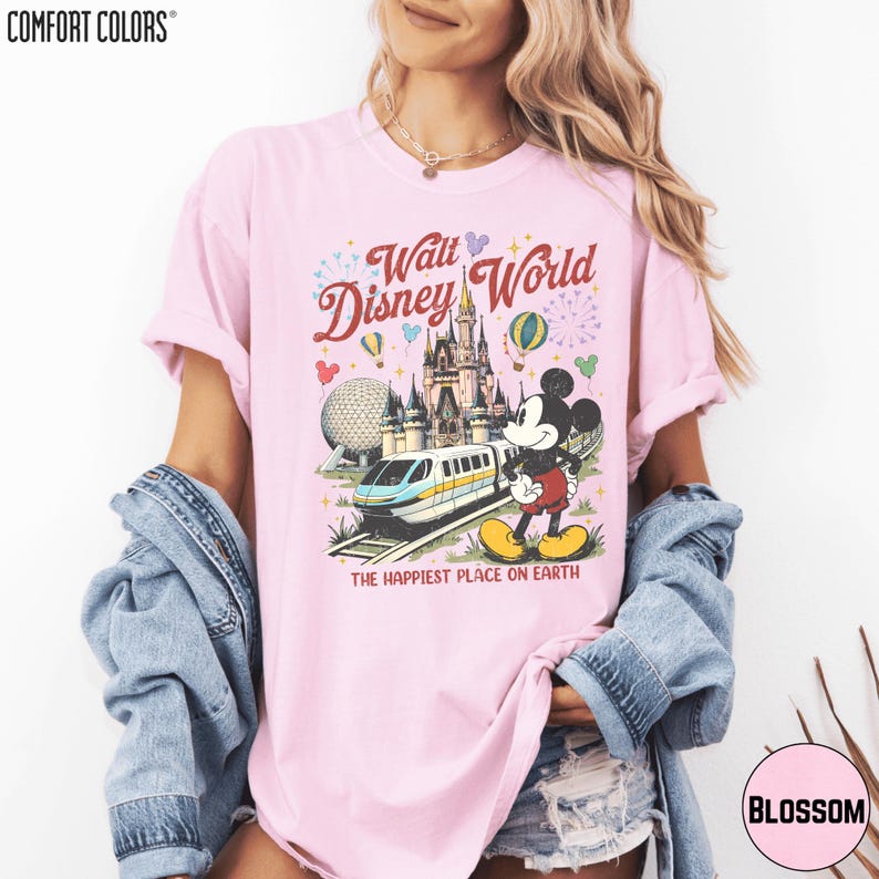 A woman wearing a pink t-shirt with a Disney World graphic and text, along with a denim jacket.