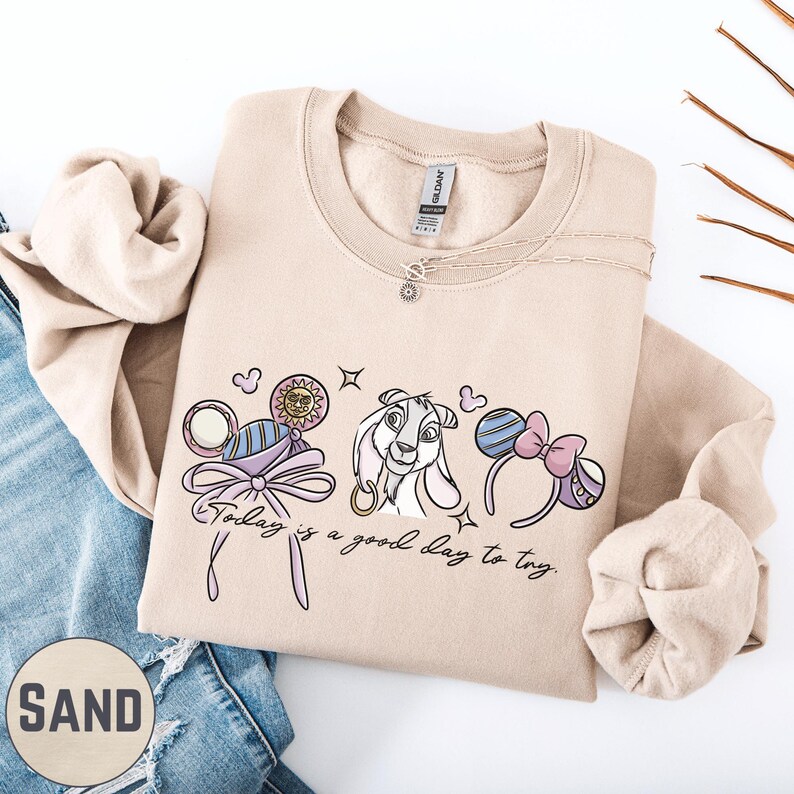 A beige sweatshirt with a graphic design featuring a cartoon character and the text "Today is a good day to try" printed on it.