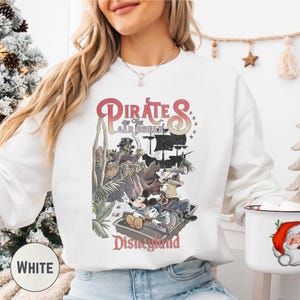 A woman wearing a white sweatshirt with a graphic of Disney characters and the text "Pirates of the Caribbean: The Caribbean" printed on it.
