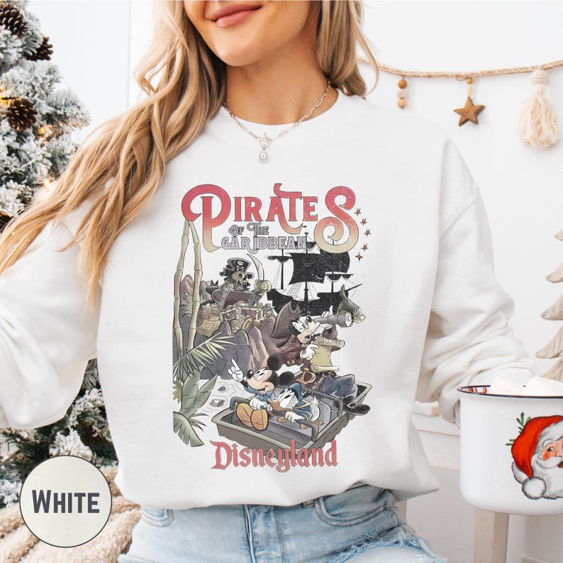 A woman wearing a white sweatshirt with a graphic of Disney characters and the text "Pirates of the Caribbean: The Caribbean" printed on it.