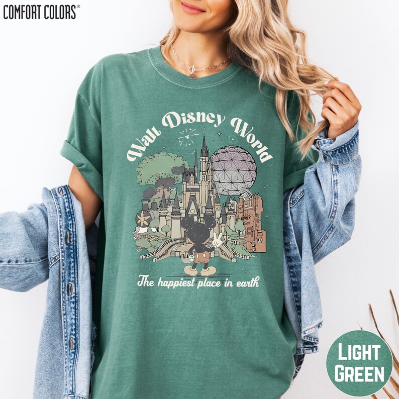 A woman wearing a green t-shirt with a graphic of Disney World and the text "The happiest place in earth" printed on it.