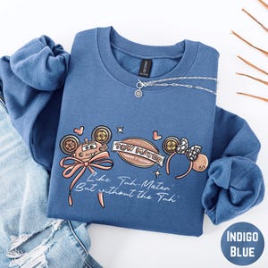 A blue sweatshirt with a cartoon character design and text printed on it, along with a necklace and some jeans.