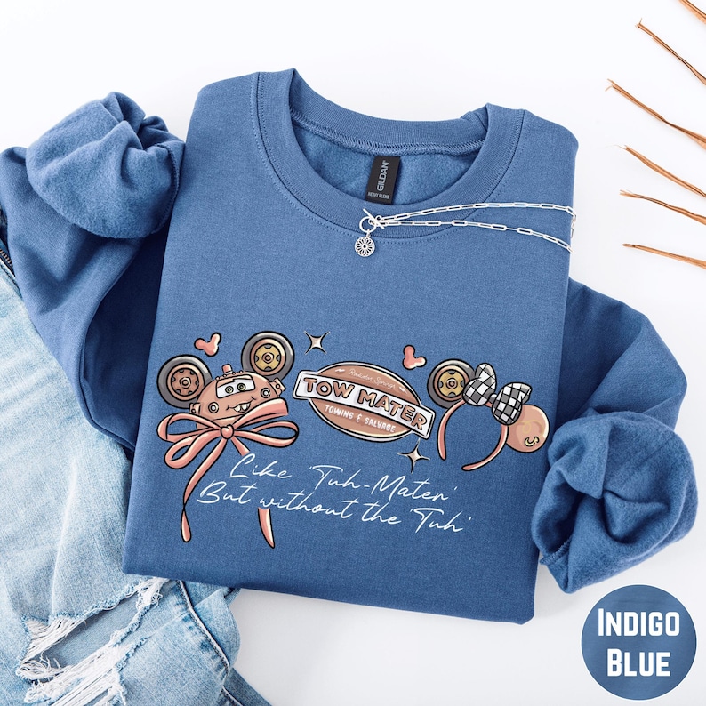 A blue sweatshirt with a cartoon character design and text printed on it, along with a necklace and some jeans.