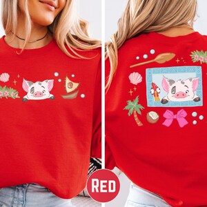 A red t-shirt with a cartoon pig design and various decorative elements, including a boat, palm tree, starfish, and other whimsical objects.