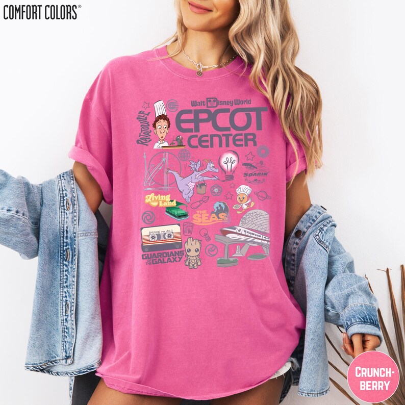 A woman wearing a pink t-shirt with various Disney-themed graphics and text, including a chef, a roller coaster, and other iconic Disney characters and landmarks.