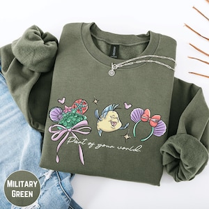 A military green sweatshirt with a graphic design featuring a cartoon fish and flowers, along with the text "Part of your world" printed on it.